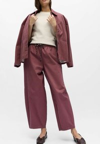 Maroon jacket over an off-white textured sweater, paired with loose-fitting maroon trousers featuring a drawstring waist and black accents.