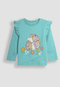 Camicia azzurra a maniche lunghe con spalle arricciate, caratterizzata da ricami di ricci e fiori in colori vivaci. Materiale in cotone morbidissimo.