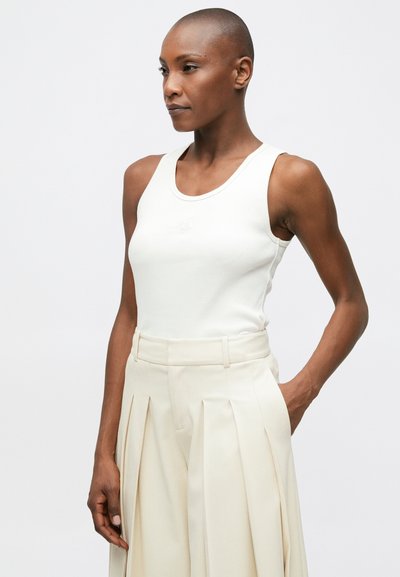 Biely rebrovaný top s okrúhlym výstrihom, skombinovaný s krémovými plisovanými nohavicami s pásom a bočnými vreckami.