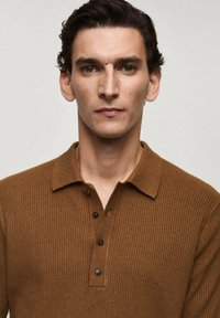Brown ribbed polo shirt with a collar and four black buttons. The fabric appears soft and textured, creating a casual style.