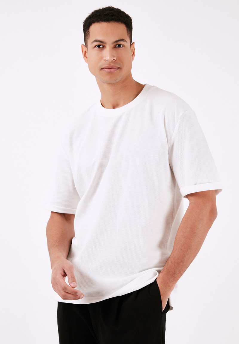 Tricou scurt cu mânecă albă, din bumbac, cu guler rotund și o textură ușor ribbed, stilizat cu o croială lejeră.