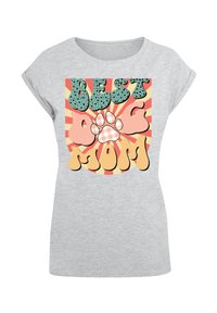 Grijze t-shirt met korte mouwen, voorzien van kleurrijke grafische tekst "BEST DOG MOM" met een pootafdruk, tegen een gestreepte achtergrond.