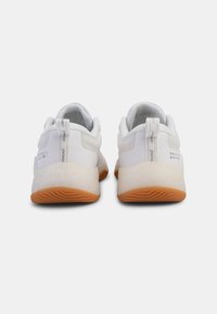White athletic shoes with a textured upper, padded collar, and rubber sole featuring a brown tread pattern. Pull tab at the back for easy wear.