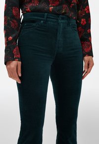 Donkerblauwe corduroy broek met een aansluitende taille en rechte pijpen, voorzien van zijzakken en een zachte textuur. Gecombineerd met een bloezen met bloemenpatroon.