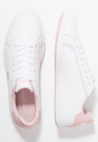 Baskets synthétiques blanches avec des accents roses. Elles comportent des lacets, un intérieur texturé et une semelle en caoutchouc rose contrastante.