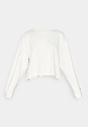 Baltas trumpintas ilgomis rankovėmis džemperis, pasižymintis laisva forma, guliuočiais rankogaliais ir mažuoju logotipu ant krūtinės. Minkšta medžiaga su sklandžiu paviršiumi.