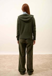 Hoodie en tricot vert foncé avec capuche, associé à un pantalon en velours côtelé vert foncé ample. Texture lisse, design simple, sans motifs visibles.