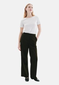 T-shirt blanc à manches courtes associé à un pantalon en velours côtelé vert olive foncé, taille haute et coupe droite. Le pantalon est doté de poches latérales et d'une texture lisse.