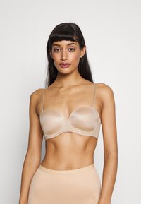 Lys beige, polstret bh med tynne, justerbare stropper. Glatt tekstur og sømløst design, med en buet silhuett for støtte.