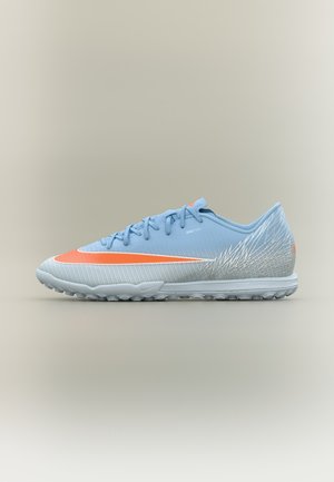 Chaussure de sport bleu clair et grise avec le swoosh Nike orange et une semelle texturée, conçue pour gazon ou surfaces artificielles.