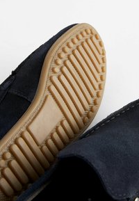 Marineblaues Wildlederschuh mit einer strukturierten Gummisohle, die Rillen und Erhebungen für besseren Halt aufweist. Die Sohle ist hellbraun und verstärkt den Kontrast zum oberen Teil.