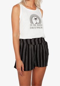 Top bianco con testo stampato nero e grafica di palme, abbinato a pantaloni corti neri con strisce bianche verticali e design plissettato.