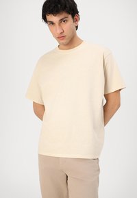 Beige bomulls T-skjorte med rund hals og korte ermene. Diskret merke logo på brystet. Løs passform med en jevn tekstur.