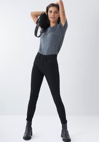 Černé skinny džíny s pěti kapsami, hladký povrch, vysoce vykrojený střih, v kombinaci se šedým tričkem s krátkým rukávem a černými kotníkovými botami.