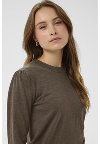 Brauner Pullover mit Rundhalsausschnitt, langen Ärmeln und dezenten Raffungen an den Schulternähten, gefertigt aus weichem Stoff mit glatter Textur.