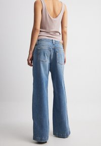 Modre široke kavbojke iz denima s staranim videzom, pet žepov in usnjenim paketom na pasu. Mehka bombažna tkanina, sproščen kroj.