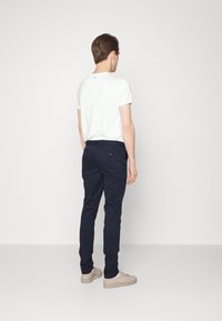 Bílá tričko a tmavě modré kalhoty, přiléhavý design, bavlněný materiál, s hladkou texturou. Obuv jsou světle béžové tenisky.