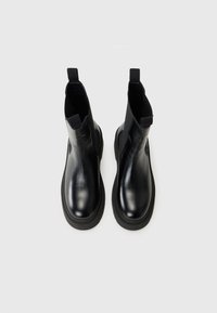 Bottines en cuir noir avec des panneaux élastiques sur les côtés et une semelle épaisse, vues du dessus sur un fond blanc uni.