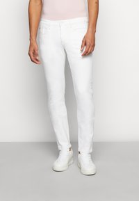 Hvide denimjeans, slim fit, med en glat tekstur. Har fem lommer og lynlås. Kombineret med hvide sneakers.