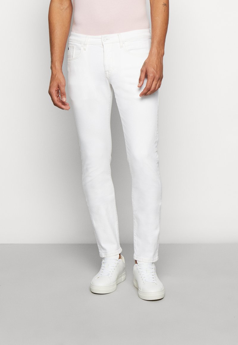 Hvide denimjeans, slim fit, med en glat tekstur. Har fem lommer og lynlås. Kombineret med hvide sneakers.