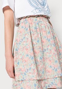 Saias florais em cores pastéis; tecido leve com um cós franzido e design em camadas. Apresenta um padrão de flores rosas e azuis.