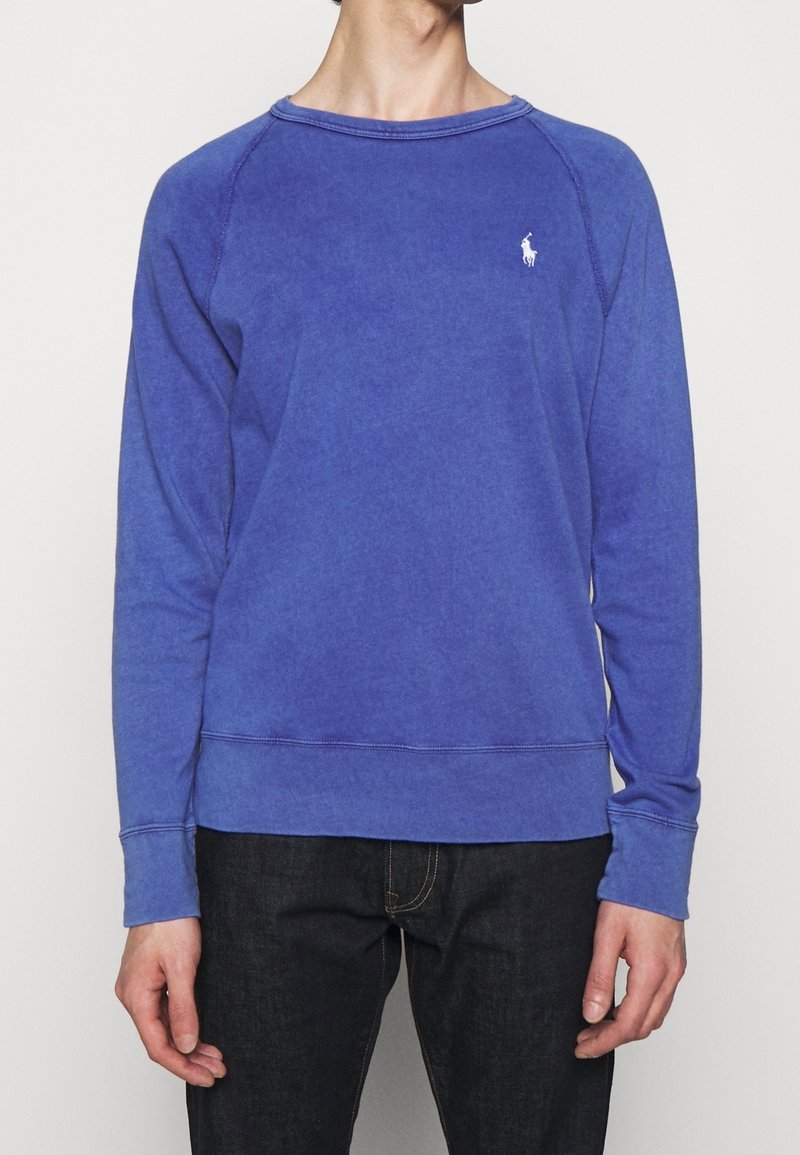 Sudadera de algodón morada con cuello redondo, puños y dobladillo acanalados, que presenta un pequeño logo bordado en el pecho. Textura suave.