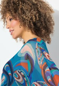 Multifarvet bluse med et flydende design i teal, koral og brune paisley-mønstre. Let, gennemsigtig stof med en løs pasform.