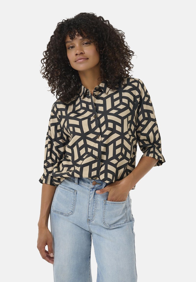 Hemd mit Knöpfen in Cremefarbe und auffälligem schwarzen geometrischen Muster. Verfügt über aufgerollte Ärmel und einen lockeren Schnitt. Kombiniert mit hellblauen Jeans.