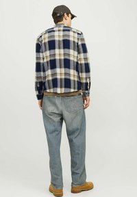 Camisa de franela a cuadros en navy, crema y gris, combinada con jeans de color azul claro. Presenta mangas largas, un dobladillo curvado y cuello estándar.
