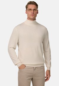 Krēmkrāsas turtlenecks džemperis mīkstā adījumā, pieguļošs dizains, ar garām piedurknēm un ribotām pieturēm, apvienots ar gaišām bēžām biksēm.