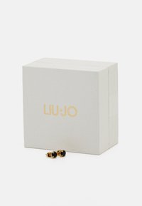 Liu Jo Ohrringe mit schwarzen Steinen, in einer goldfarbenen Hardware gefasst, präsentiert neben einer hellgrauen Verpackung mit goldenem Logo.