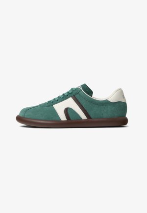 Zapatilla deportiva de ante verde con detalles en blanco y marrón, puntera redondeada y suela plana de goma marrón. Cuenta con cierre de cordones y cuello acolchado.