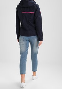 Granatowa kurtka z kapturem, różowymi akcentami i detalem na zamek z tyłu; do tego jasnoniebieskie skrócone dżinsy i białe buty.