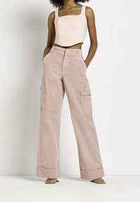 Světle růžový cropped top s čtvercovým výstřihem a strukturovaným designem, spárovaný s širokými cargo kalhotami s bočními kapsami a ohrnutým lemem.