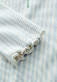 Tissu rayé bleu clair et crème avec une texture côtelée, arborant un détail de poignet froncé au bout de la manche.