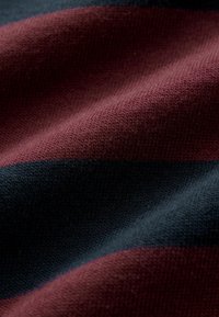 Țesătură tricotată cu dungi orizontale în nuanțe de burgund și albastru închis. Textură fină cu cusături vizibile și detalii de tricotaj rafinate.