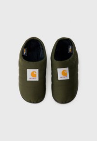 Oliwkowozielone, ocieplane kapcie z pikowanym wzorem, czarną płaską podeszwą i białą naszywką z logo Carhartt na cholewce. Miękka podszewka wewnętrzna.