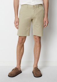 Beige cotton shorts with a slim fit, flat front, and side pockets. Styled with brown suede sandals.