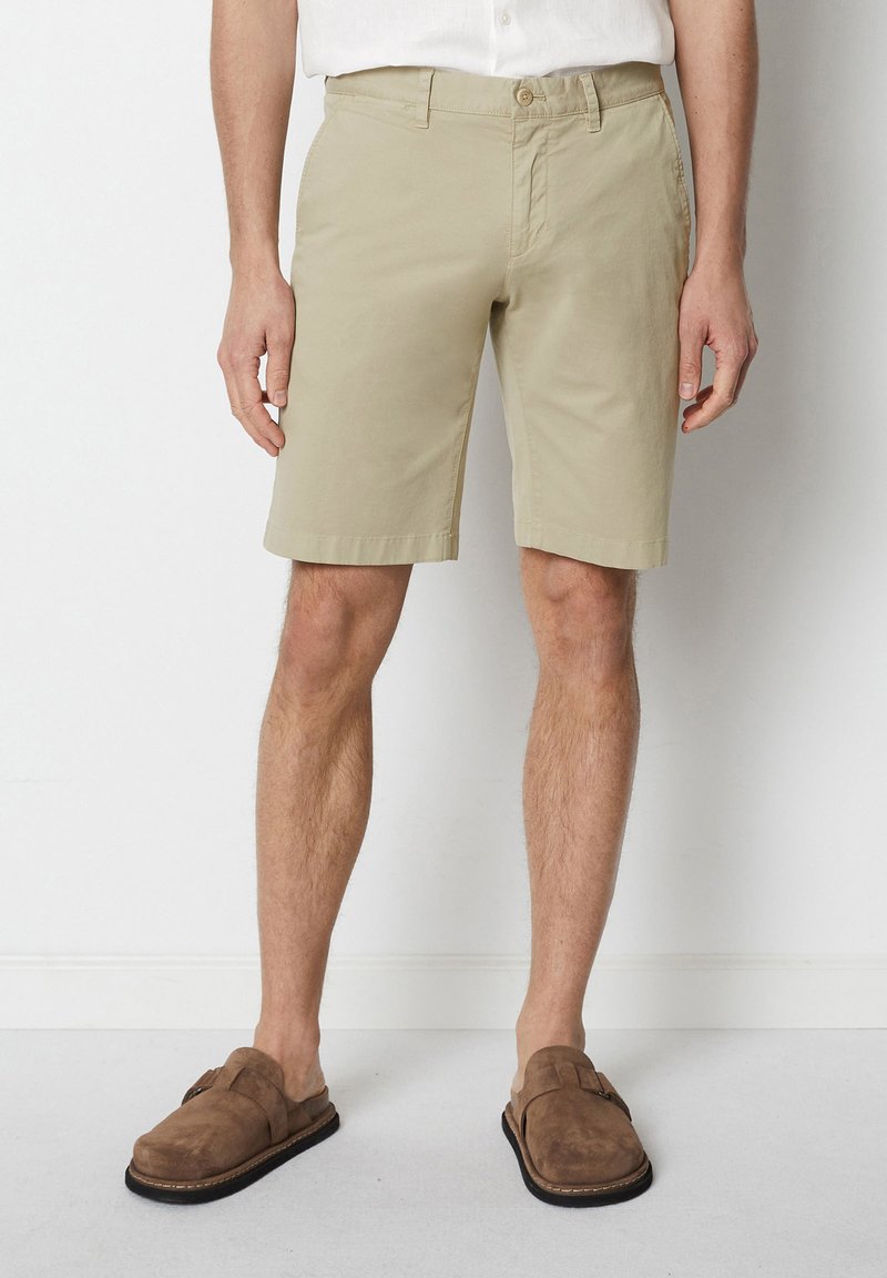 Beige cotton shorts with a slim fit, flat front, and side pockets. Styled with brown suede sandals.