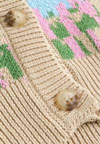 Strickjacke aus Strickstoff in Beige mit mehrfarbigem Blumenmuster. Verfügt über eine strukturierte Oberfläche und einen runden, hellbraunen Knopf.