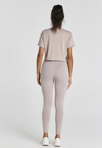 Vaalean beige lyhyt t-paita yhdistettynä vaaleanpinkin kiristyslegginseihin, joissa on struktuuripinta. Mallilla on valkoiset tennarit.