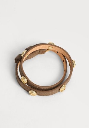 Bracciale avvolgente in pelle marrone con borchie decorative dorate, arrotolato su una superficie chiara. Nessuna persona o altro oggetto presente.