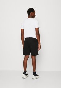 Czarne szorty o gładkiej teksturze, z tylną kieszenią. Połączenie z białą koszulką i czarnymi trampkami.