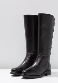Botas de cuero negras hasta la rodilla con textura suave, punta redonda, cremallera lateral y detalles de botones en el exterior. Tacón bajo apilado.
