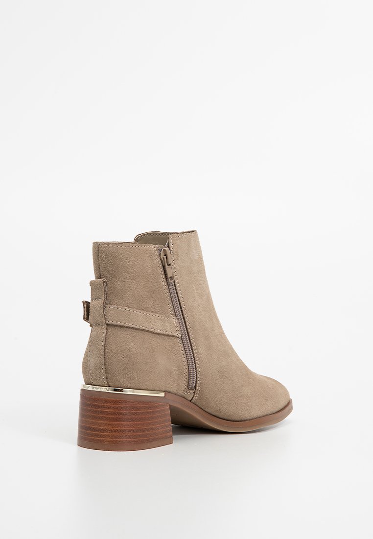 Bottines en suede beige avec un bout arrondi, une fermeture éclair sur le côté et un talon bloc brun avec un accent doré à la base. Texture lisse.