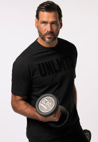 Camiseta deportiva negra con diseño en relieve "UNLMTO", sostenida por una persona que agarra un mancuerna negra con una etiqueta de peso plateada.