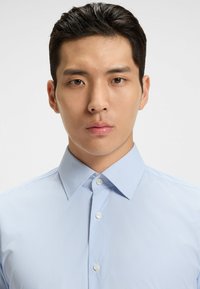 Ljusblå randig skjorta med knappar och en strukturerad krage. Tyget verkar slätt med fina vertikala linjer.