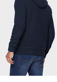 Mörkblå stickad huvtröja med ribbat mönster, med huva och muddar. Kombineras med jeans i denim, som visar en klassisk passform och fickdesign.