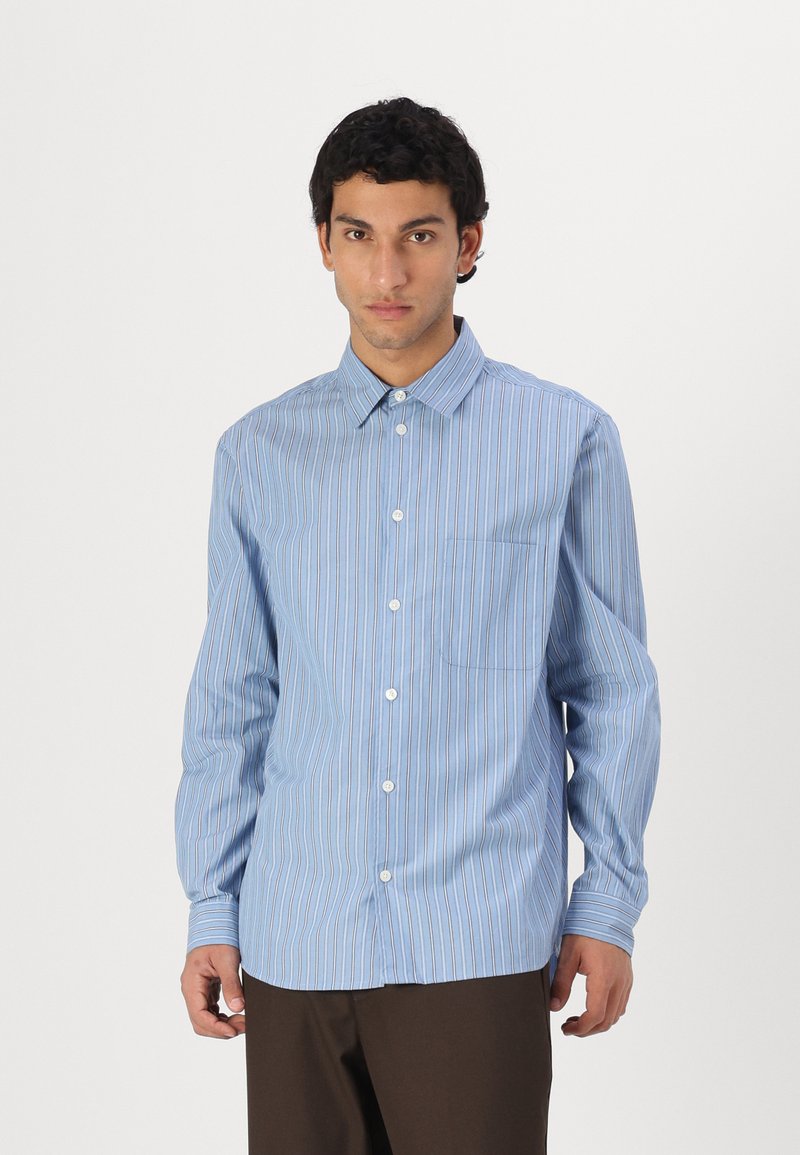 Camisa de botones azul claro con rayas verticales blancas, con cuello puntiagudo, mangas largas y un bolsillo en el pecho.