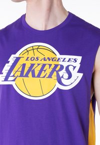 Μωβ αμάνικη μπλούζα με κίτρινα διακοσμητικά, που διαθέτει γραφικό μπάσκετ και κείμενο "Los Angeles Lakers" σε λευκό και μωβ. Μαλακό βαμβακερό ύφασμα.